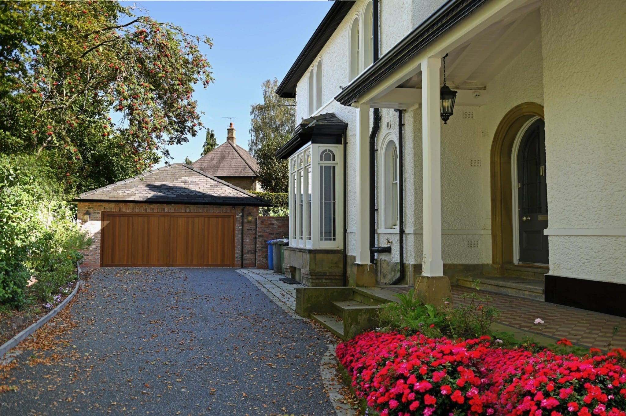 a driveway leading to a house with red flowers.