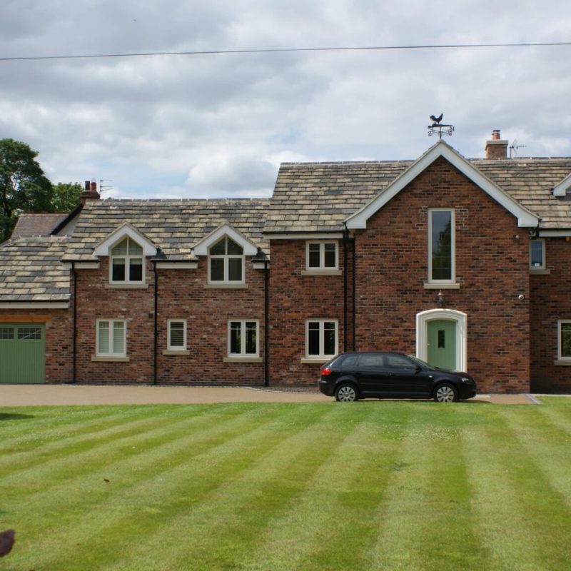 A large brick house undergoing restoration, with a car parked in front of it.